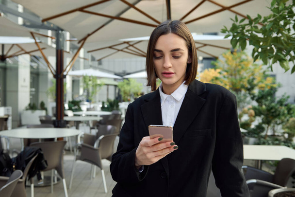 Self-confident woman holding mobile phone smartphone, typing text messages, messaging, swiping web page. Business, finance, online remote work, online shopping, communication and connection concepts - Valokuva, kuva