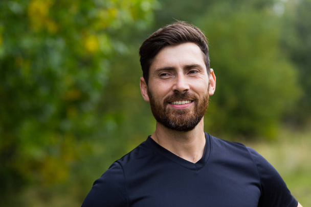 Close up portrait young happy bearded man standing in nature between forest trees relaxes, breathes fresh air closing his eyes. Male enjoys a life of peace calm, quiet in the park. Outdoors. Happiness - Foto, Bild