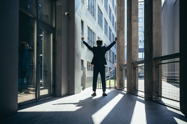Successful african american businessman with arms up celebrating victory. Concept: success, career growth, victory, freedom. silhouette business man on the background a modern office building. outside - Foto, afbeelding
