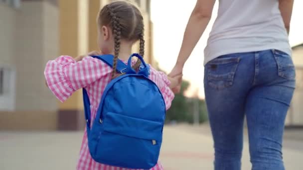 dziewczynka z plecakiem trzyma matkę za rękę i chodzi do szkoły, dziecko z mamą chodzi do szkoły na podwórku szkolnym, dziecko z torbą szkolną śpieszy się na pierwszą lekcję, edukacja przedszkolna przygotowawcza - Materiał filmowy, wideo