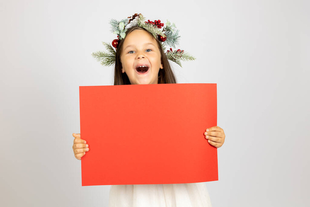 portrait of laughing, cheerful girl in Christmas wreath holding red banner isolated on white background - Photo, Image