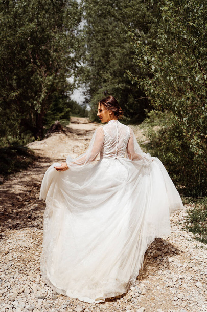 woman in wedding dress walks along mountain path between trees. view from back.  - Fotoğraf, Görsel