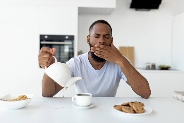 Black guy pouring coffee away from cup and yawning - Foto, imagen