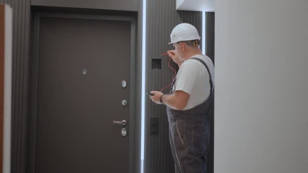 Muž elektrikář kontroluje napětí v síti s drátovým testovačem připravujícím instalaci chytrého domu. Stavitel na opravě bytu se světelnými liniemi - Záběry, video