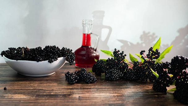 Ripe elderberry squeezed in syrup in a bottle. Natural black berry juice. Homeopathy copy space. - Фото, зображення