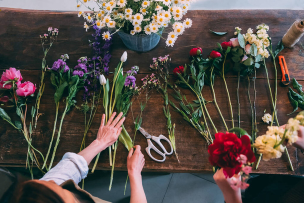 Florista hace un ramo moderno de moda de diferentes flores sobre un fondo de mesa de madera. Vista desde arriba - Foto, imagen