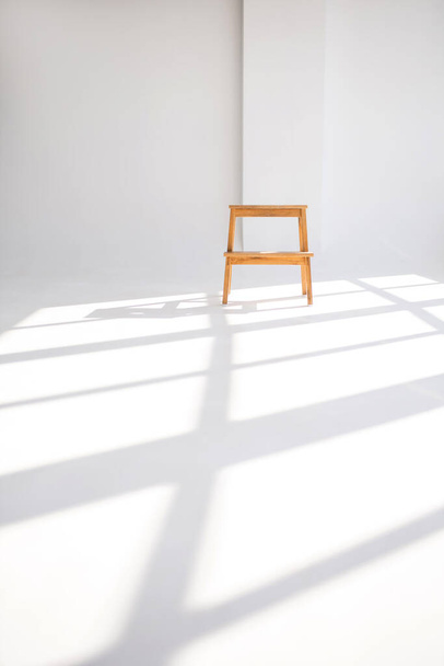Wooden chair in a white room with shadows from the windows. Stylish minimalism in the form of a single chair in a clean white room. Shadows on the floor from the windows near the chair - Photo, Image