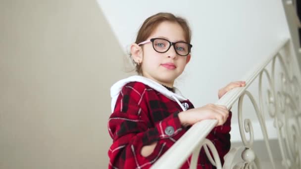 Portrait d'une petite fille dans un pull rouge avec des verres. Souriant et agitant la main - Séquence, vidéo
