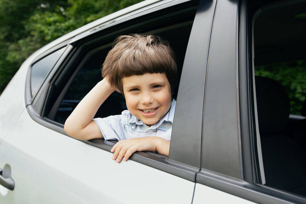 Fröhlicher kleiner Junge schaut während einer Fahrt aus dem Autofenster - Foto, Bild
