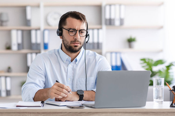 Skoncentrowany poważny dojrzały biały facet w okularach, słuchawki pracują na laptopie we wnętrzu salonu - Zdjęcie, obraz