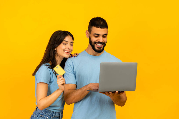 Concepto de compras online. Feliz pareja árabe joven usando computadora portátil, dama con tarjeta de crédito de débito dorado - Foto, imagen