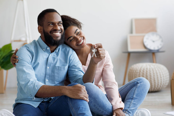 Glad millennial african american husband and wife moving to new apartment, sits among boxes - Photo, Image