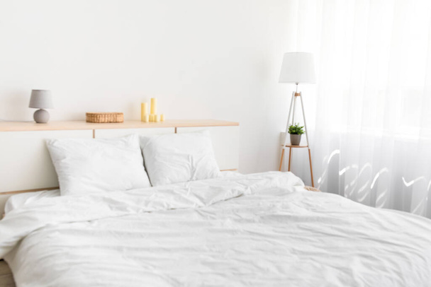 Cama doble con ropa de cama cómoda, lámpara con planta, muebles - Foto, imagen