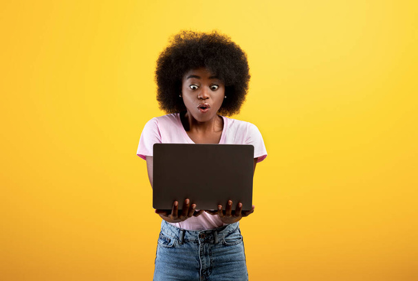 Schockinhalt. Überwältigte schwarze Dame schaut auf Laptop-Bildschirm, erhält Nachrichten oder leidet unter Internet-Betrug - Foto, Bild