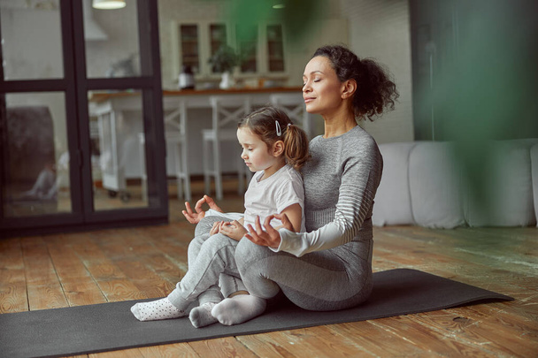 Calm mother and daughter doing yoga together - Photo, Image