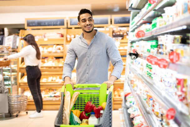 Arab Guy ψώνια Παντοπωλεία με τα πόδια Επιλέγοντας προϊόντα στο σύγχρονο σούπερ μάρκετ - Φωτογραφία, εικόνα