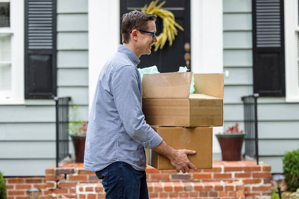 Мужчина и отец, держащие коробки рядом с маленьким голубым домиком, готовятся переехать в новый дом. - Фото, изображение