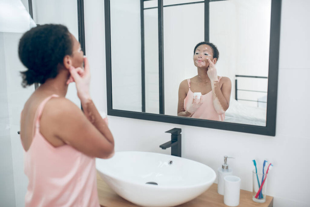 A cute young woman applying moisturizing cream on her face - Фото, зображення