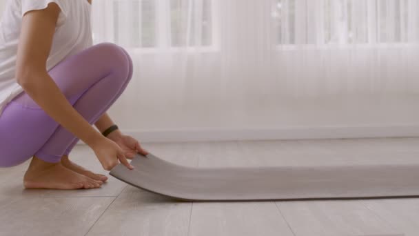 Egy ázsiai nő közelről közelíti meg a lábtörlőjét, és készül jógázni. Otthon edz a padlószőnyegen a korai napfényben.. - Felvétel, videó