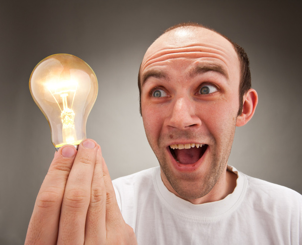 Homem surpreso segurando lâmpada de iluminação
 - Foto, Imagem