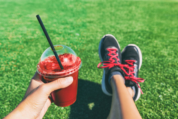 Chica bebiendo remolacha roja o batido de frutas taza de plástico durante el entrenamiento de fitness. Jugo de desintoxicación saludable mujer sosteniendo zapatos para correr de ducha de bebida en foto selfie de alimentos. Deporte estilo de vida activo - Foto, Imagen