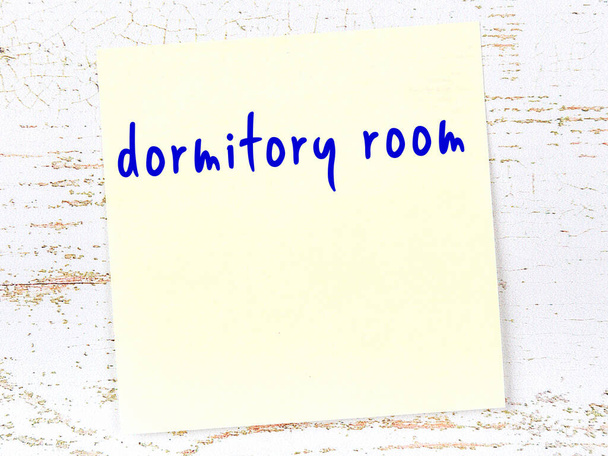 Yellow sticky note on wooden wall with handwritten inscription dormitory room - Photo, Image