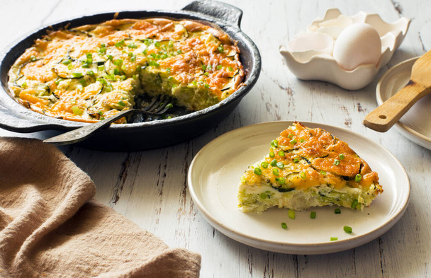 Cheesy zucchini, potatoes and greens casserole in black cooking tray on white wooden  background close up - 写真・画像