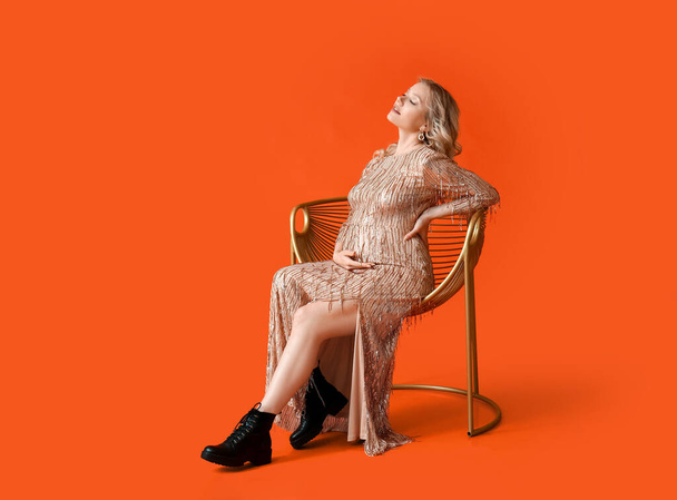 Stylish young pregnant woman sitting in chair on red background - Photo, Image