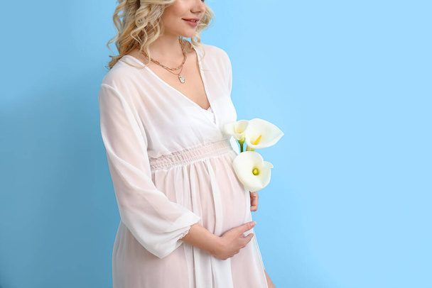 Young pregnant woman with calla lilies on blue background - Zdjęcie, obraz