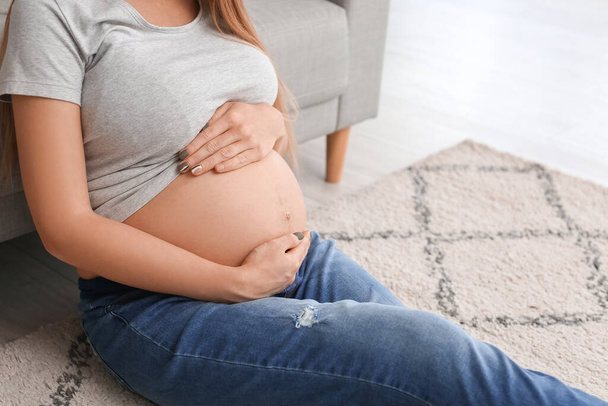 Jonge zwangere vrouw zit op de vloer thuis, close-up - Foto, afbeelding