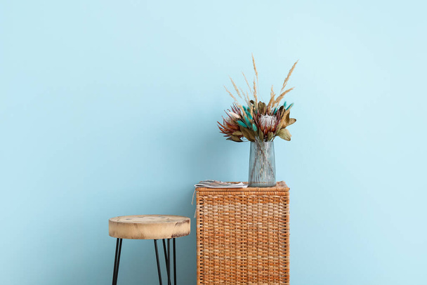 Ваза з красивими сушеними квітами і журналом на плетеному кошику біля синьої стіни
 - Фото, зображення
