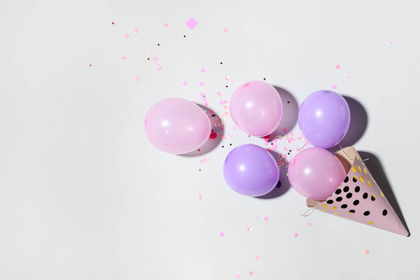 Party hat with beautiful balloons and confetti on light background - Photo, Image