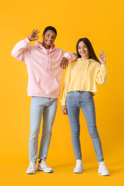 Stylish young couple in hoodies showing OK on yellow background - Fotografie, Obrázek