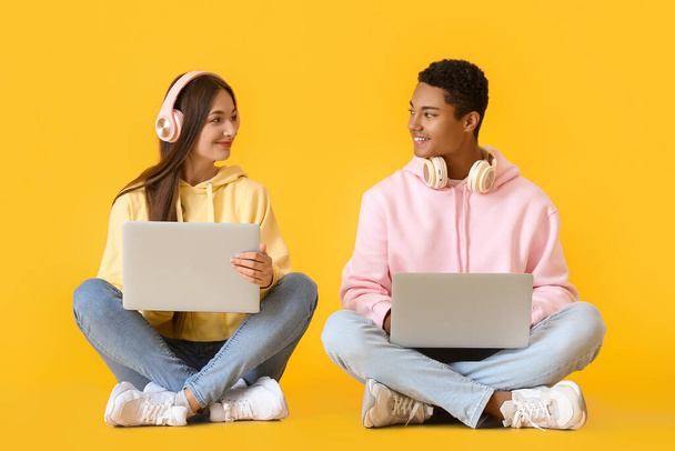 Κομψό νεαρό ζευγάρι με κουκούλες χρησιμοποιώντας φορητούς υπολογιστές σε κίτρινο φόντο - Φωτογραφία, εικόνα