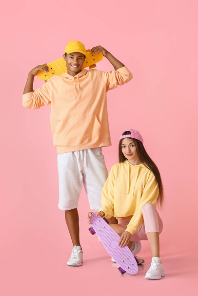Stylish young couple of skaters in hoodies on pink background - Фото, изображение