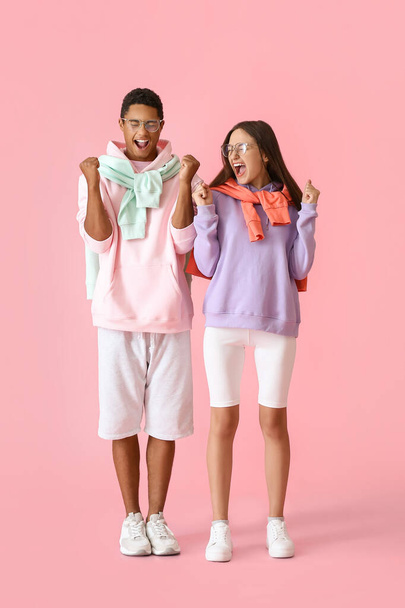 Emotional stylish young couple in hoodies on pink background - Foto, afbeelding