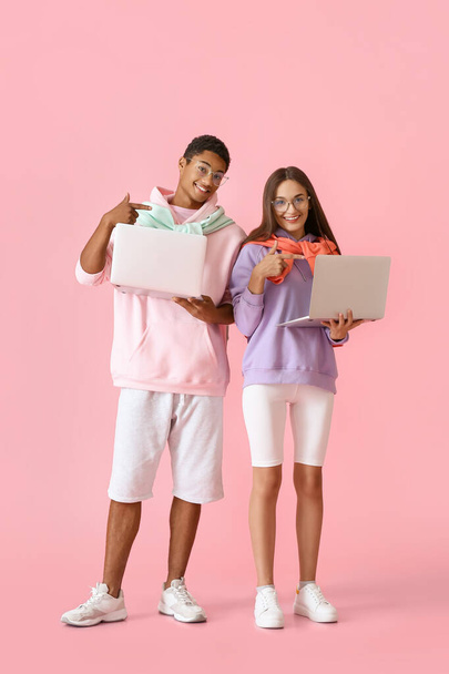 Stylish young couple in hoodies with laptops on pink background - Photo, Image