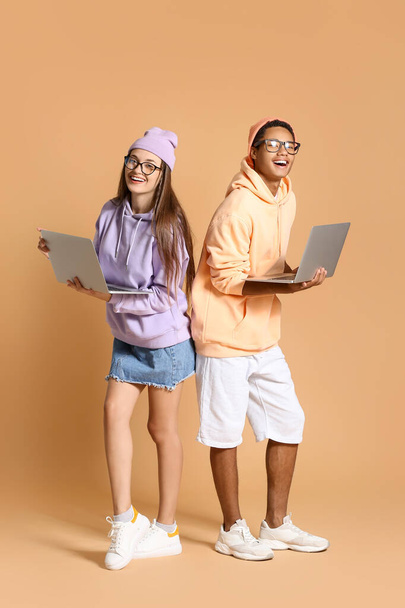 Élégant jeune couple en sweat à capuche en utilisant des ordinateurs portables sur fond beige - Photo, image