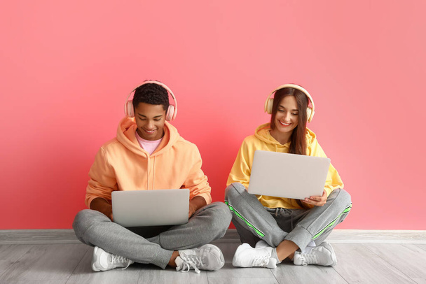 Stylish young couple in hoodies using laptops near pink wall - Fotoğraf, Görsel
