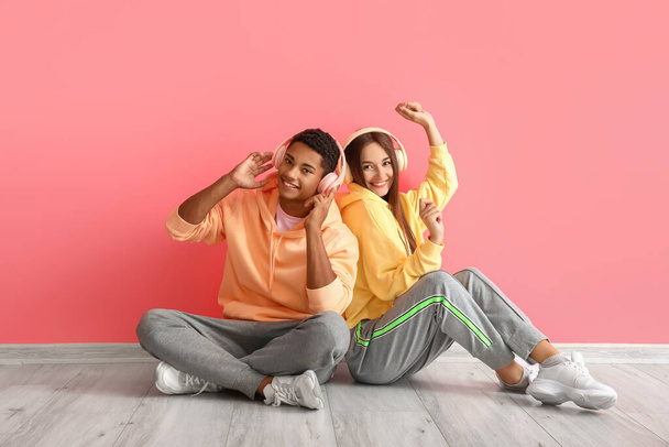 Стильная молодая пара в толстовках с наушниками возле розовой стены - Фото, изображение
