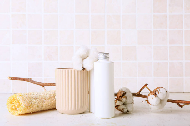 Bottle of cosmetic product, sponge and cotton branch on table against tile wall - Photo, Image