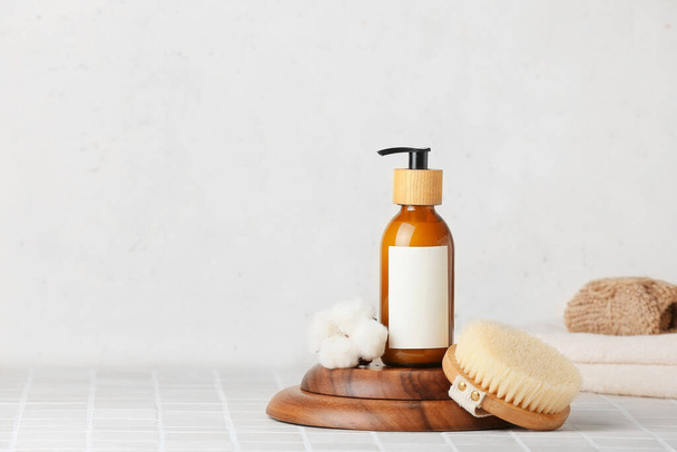 Composición con botella de producto cosmético, cepillo de masaje y flor de algodón sobre fondo claro - Foto, Imagen