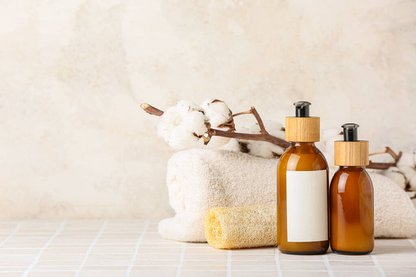 Bottles of cosmetic products, towel, sponge and cotton branch on tile table against light background - Photo, Image