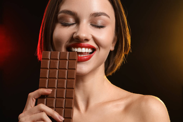 Beautiful woman with sweet chocolate on dark background - Photo, Image