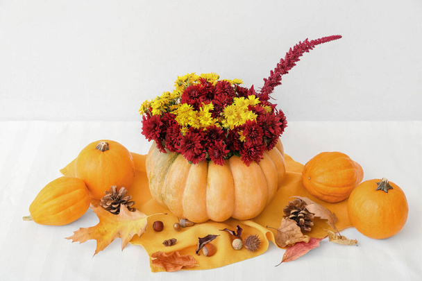Beautiful bouquet of autumn flowers in pumpkin on table near white wall - Photo, Image