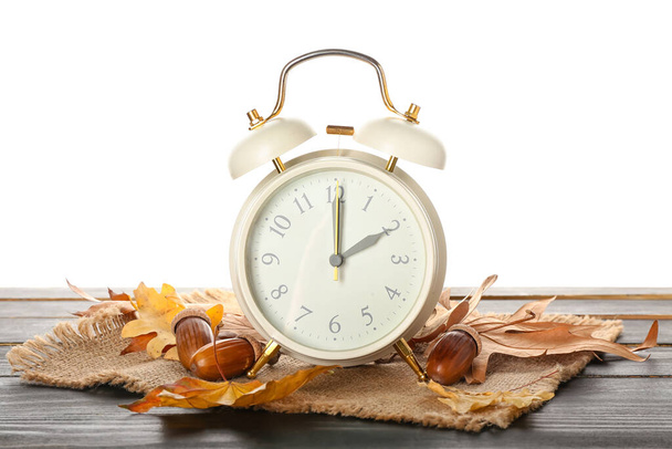 Relógio de alarme, bolotas e folhas de outono na mesa contra fundo branco. Fim do tempo de verão - Foto, Imagem