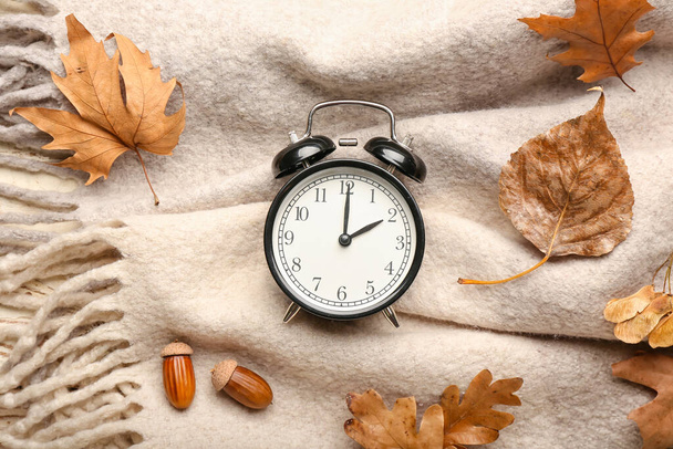 Alarm clock and autumn leaves on scarf. Daylight saving time end - Photo, Image