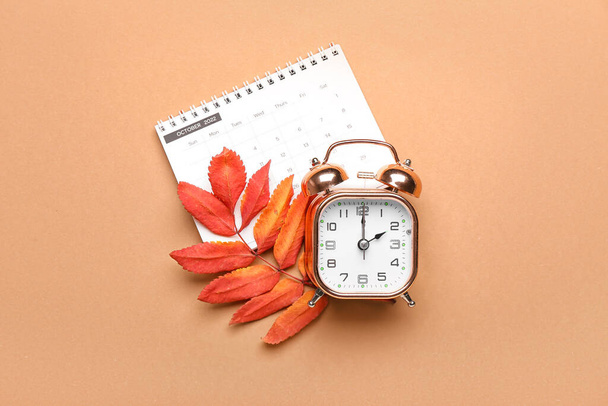 Alarm clock, calendar and autumn leaves on color background. Daylight saving time end - Photo, Image