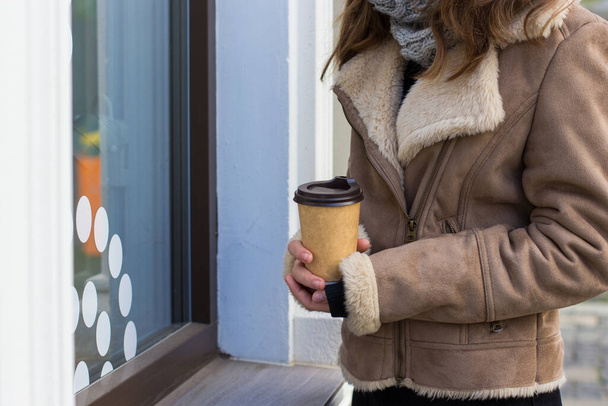 Mädchen in braunem Mantel steht mit Kaffee zum Mitnehmen auf der Straße - Foto, Bild