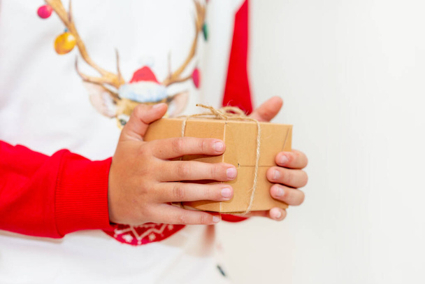 Young boy hands in pullover holding Christmas gift box on gray background.Christmas and New Year banner.Copy space. - Фото, зображення